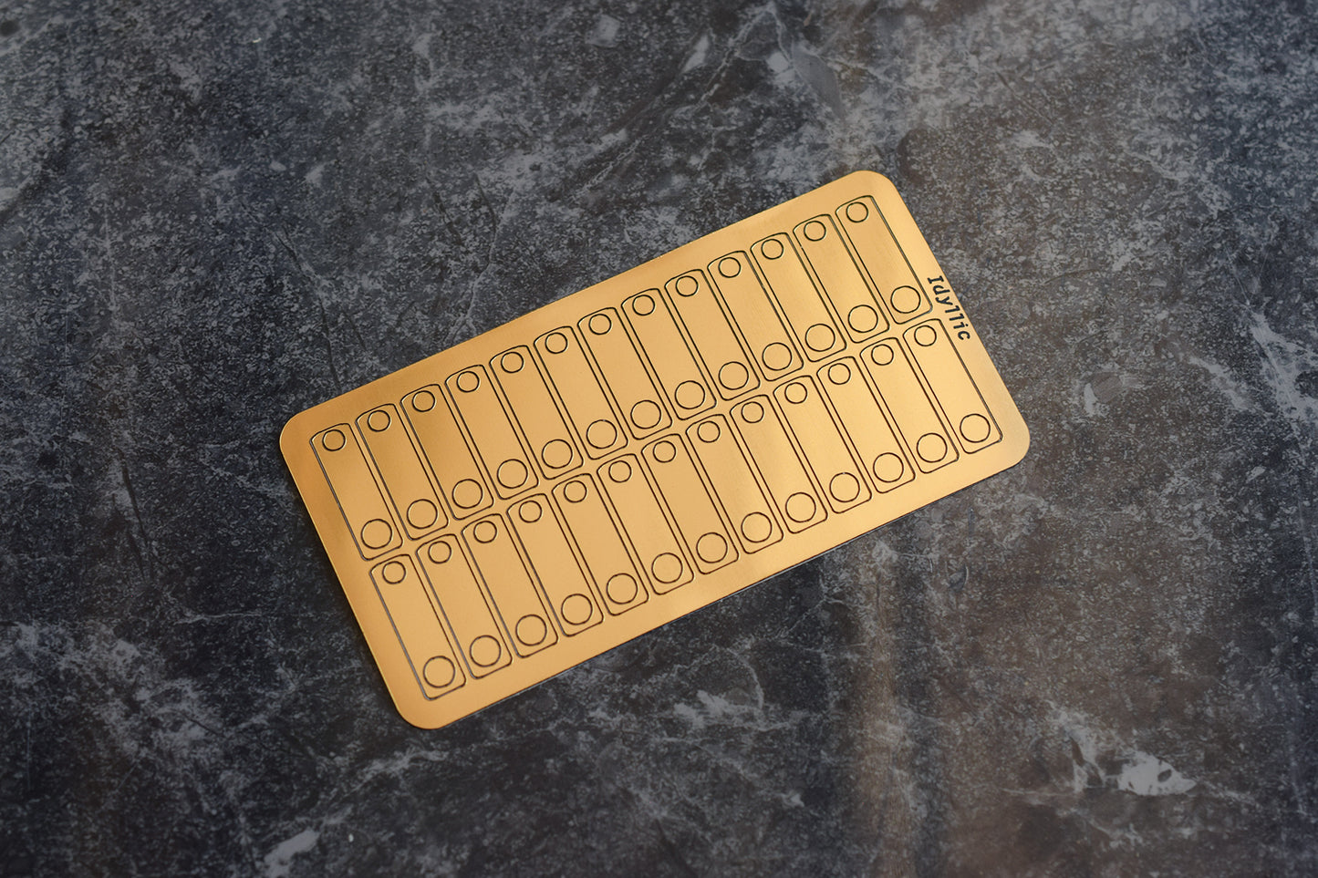 A sheet of gold-colored adhesive stabiliser shims for keyboard PCBs on a textured background.